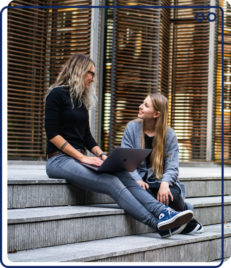 Two people working on their laptops and sitting outside on steps