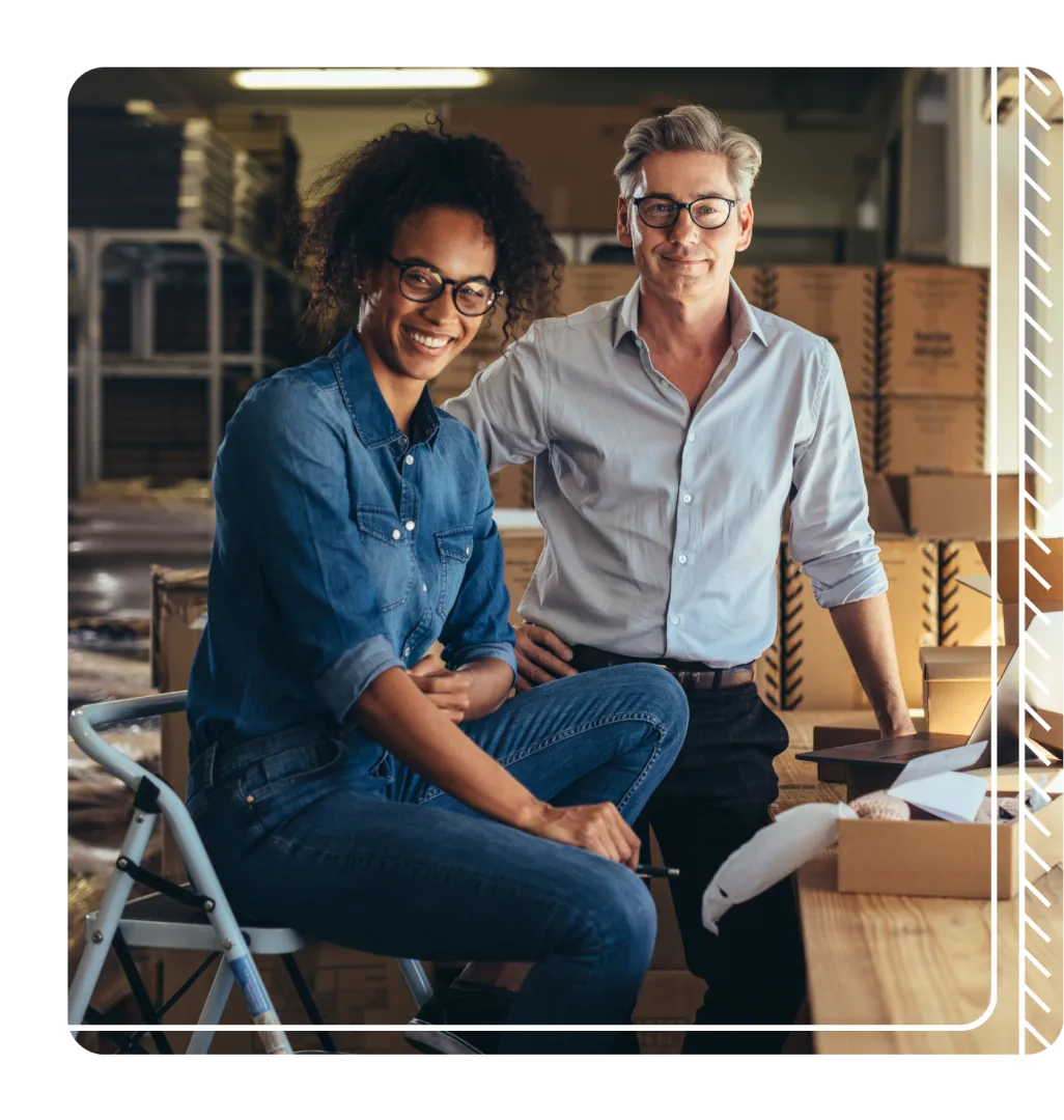Man and woman working at a desk stop to smile at the camera