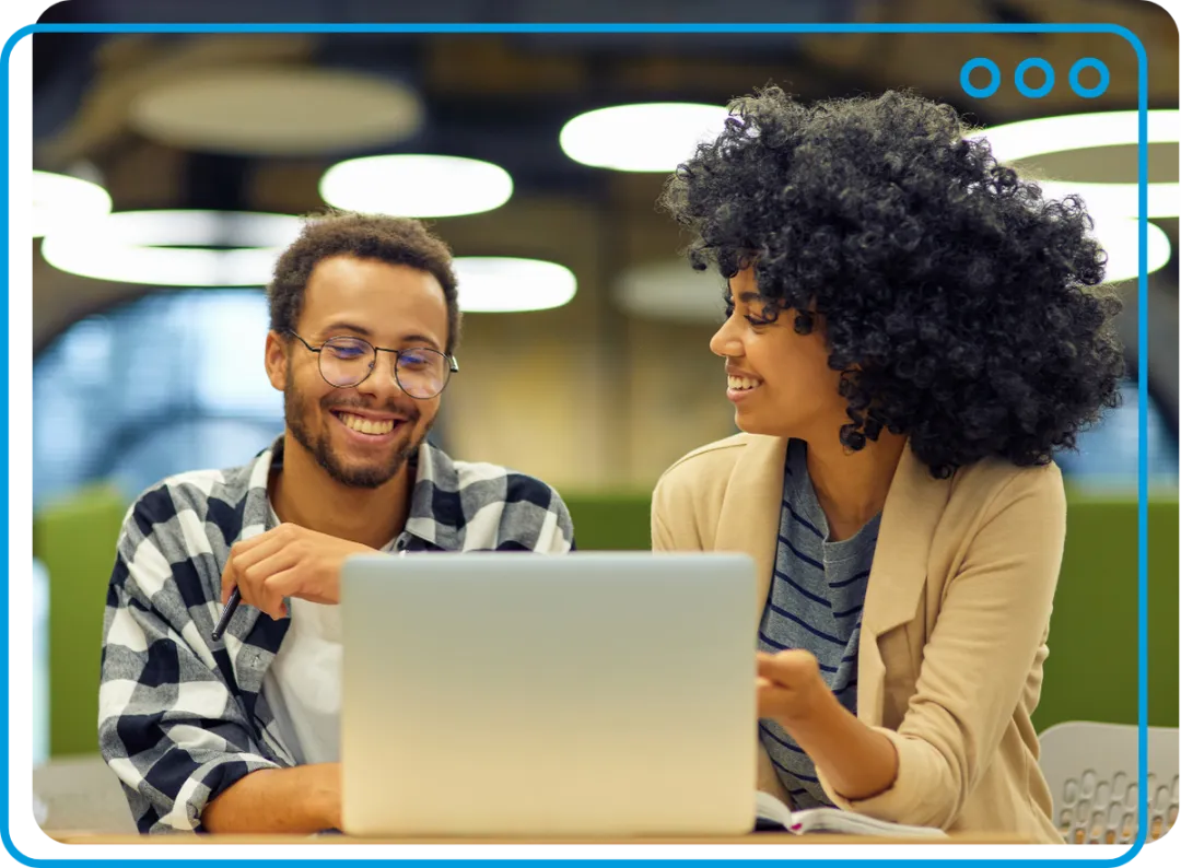A man and a woman at a laptop in an office, smiling and working together