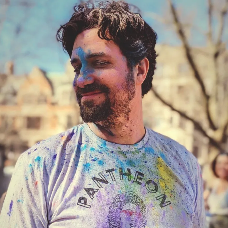 Josh Koenig - Man in a t-shirt covered in brightly colored paint.