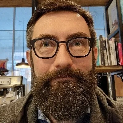 Kristof Van Tomme - Man with large beard and glasses looking up thoughtfully.
