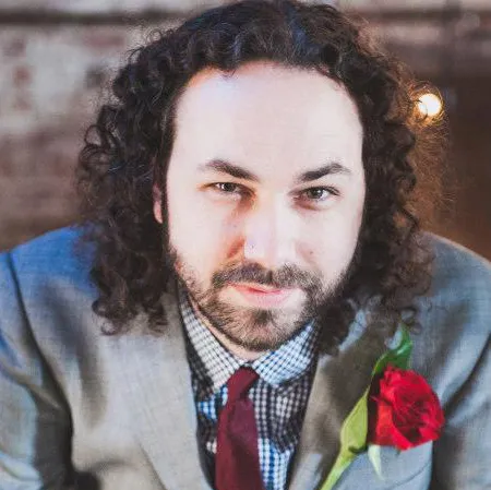 Jonathan Bourland - Man with curly brown hair and a beard. He is in a jacket and tie with a rose on his lapel.
