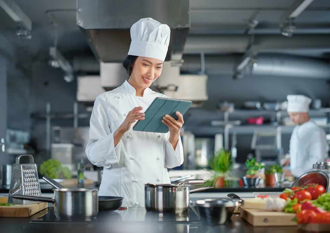Chef in a restuarant kitchen holds an ipad