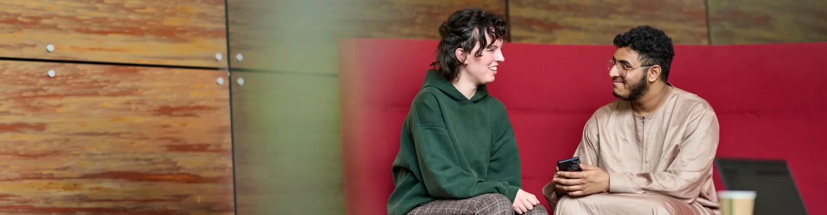 Two students talking while seated on a red upholstered bench