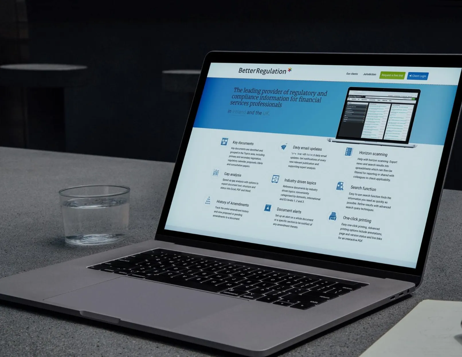 A laptop on a desk displaying the BetterRegulation.com homepage with the regulatory compliance hero banner and feature grid for financial services professionals in Ireland and the UK.