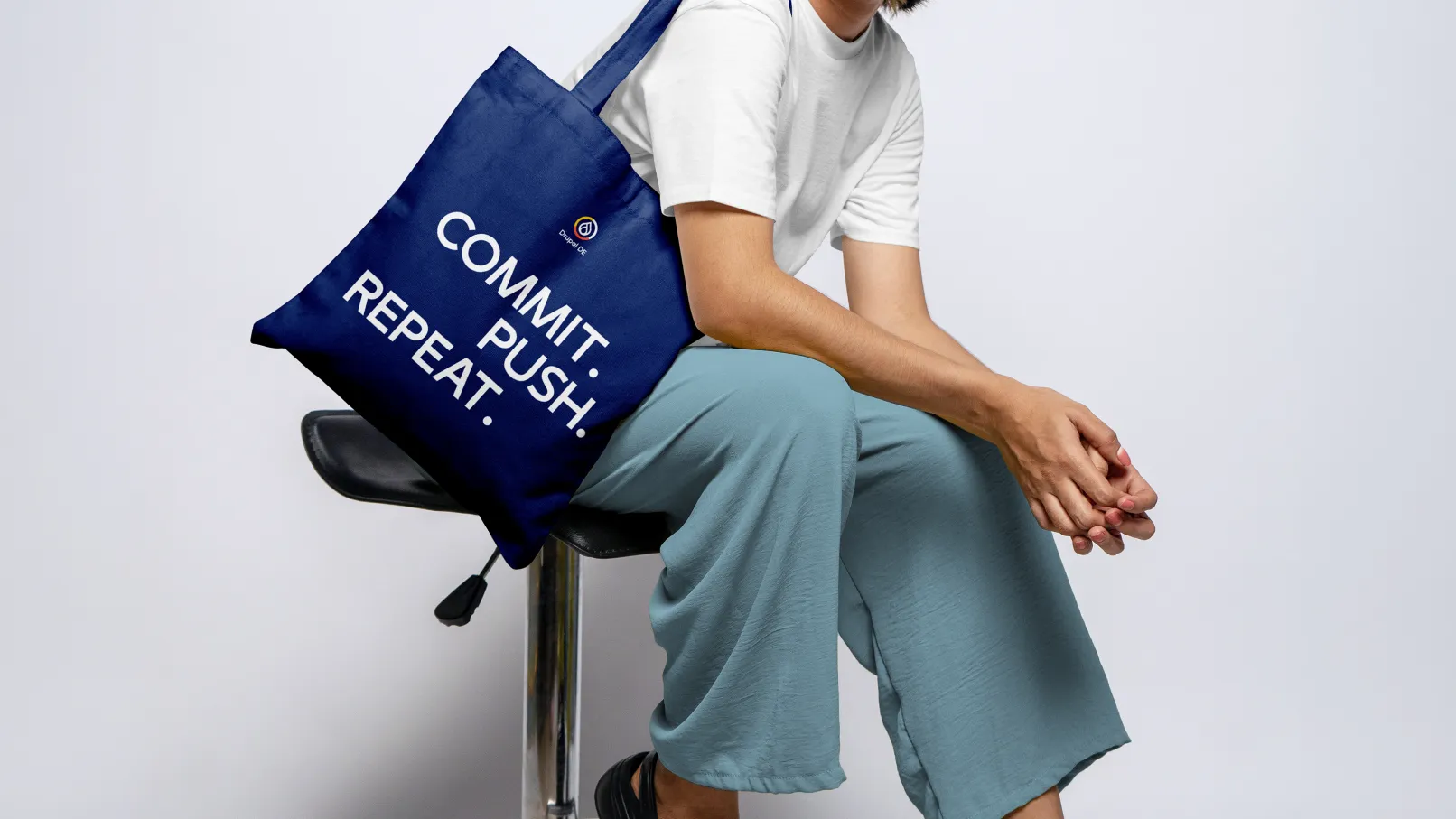 A person is sitting on a chair with a blue cloth bag featuring white text