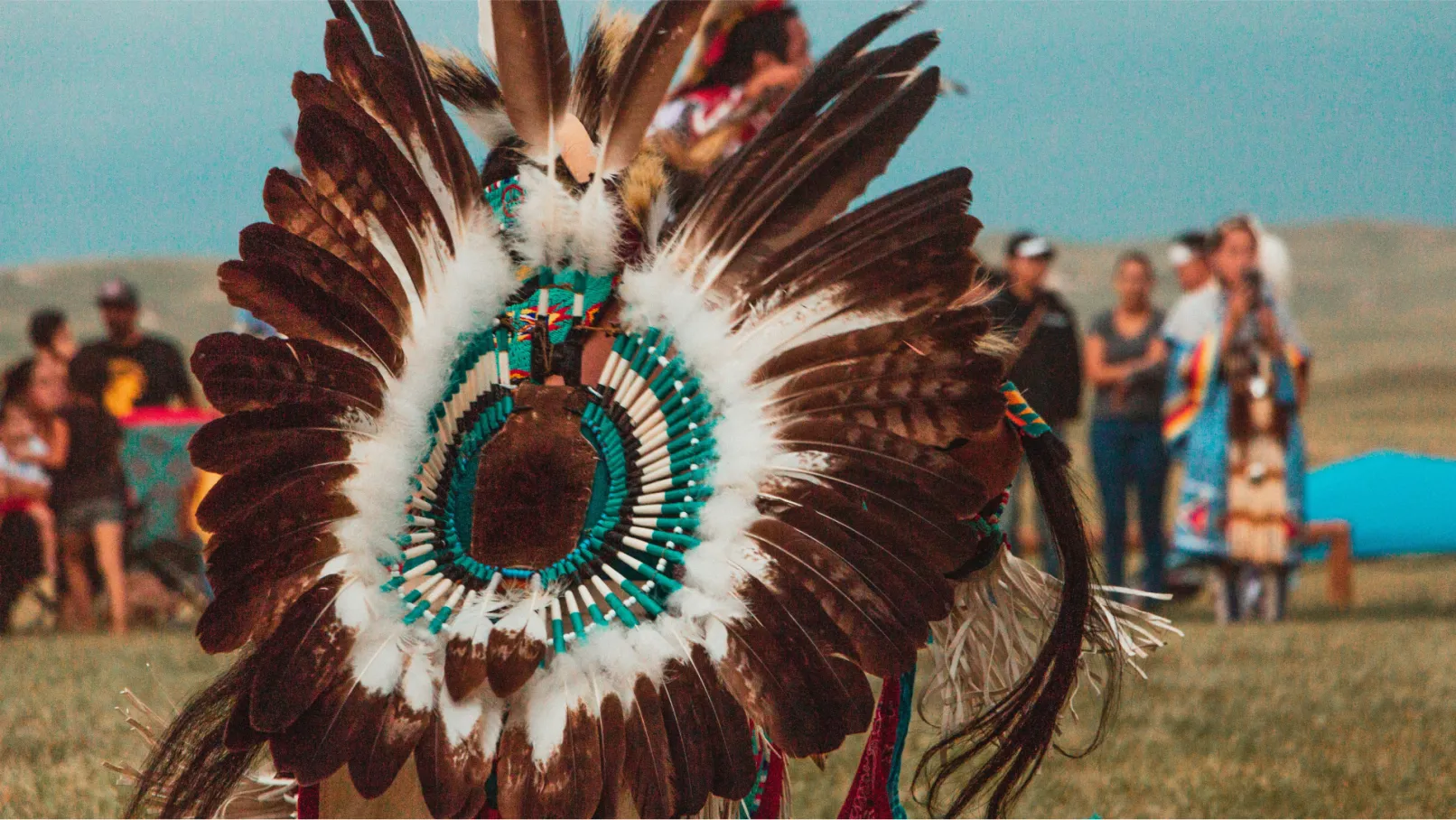 Person wearing traditional Indigenous feather regalia dancing at an outdoor cultural gathering.