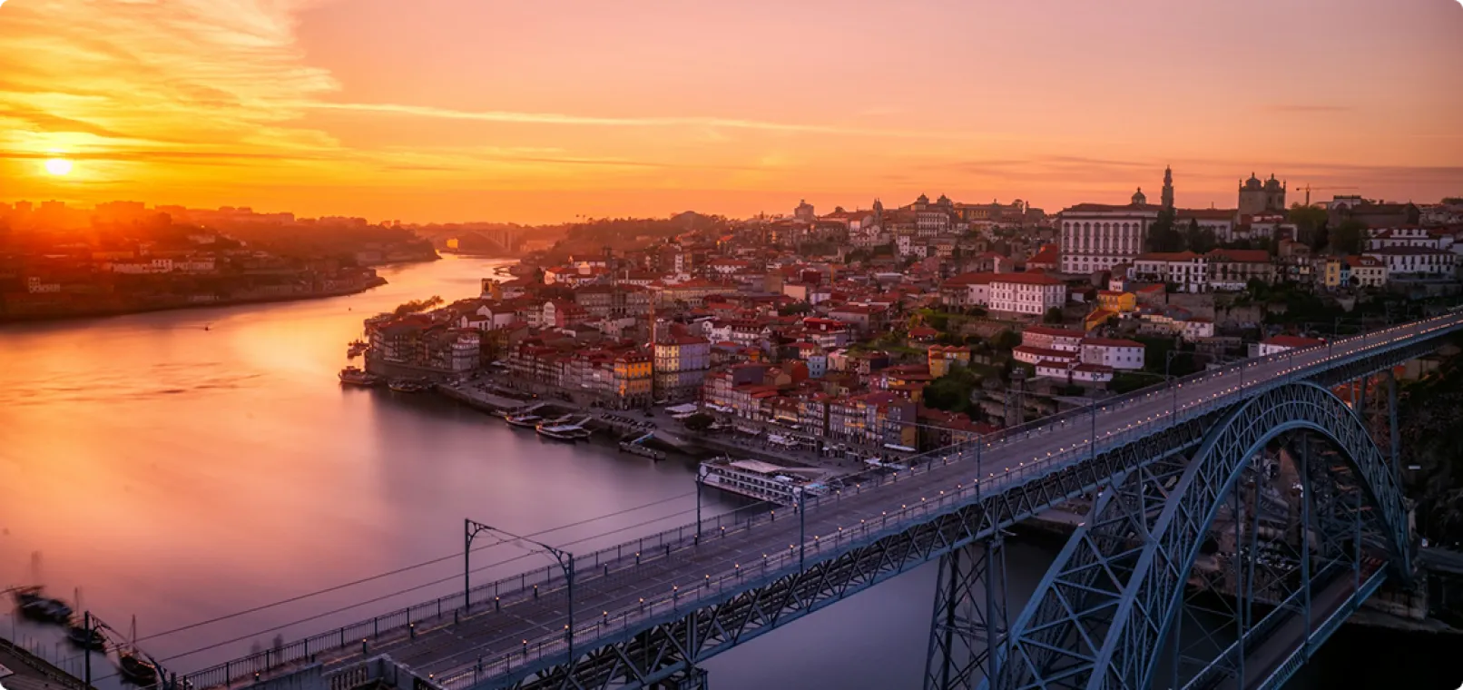Sunset over a city with a large river, and bridge in the foreground