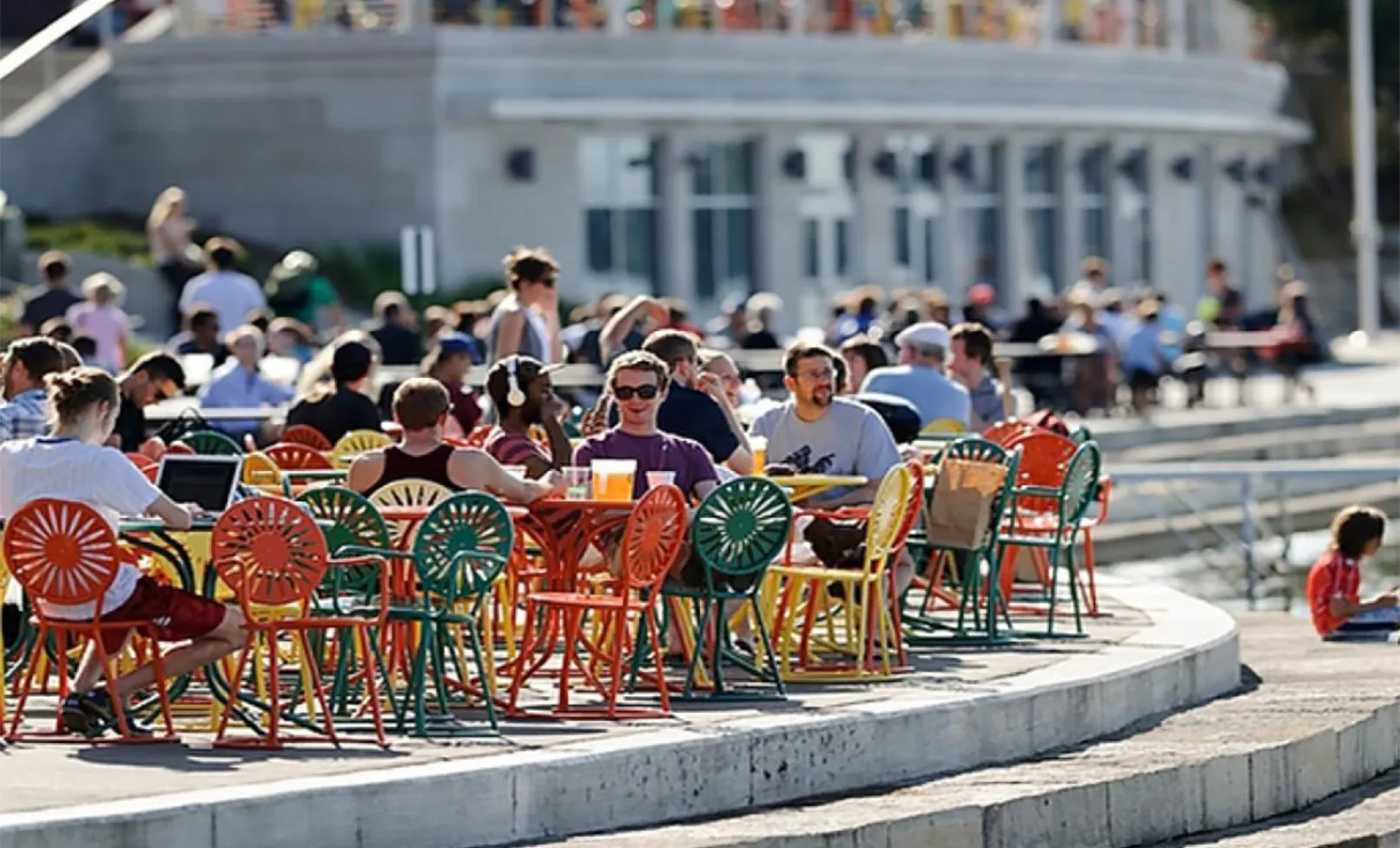 college students sitting at various tables and colorful chairs outside of the student union